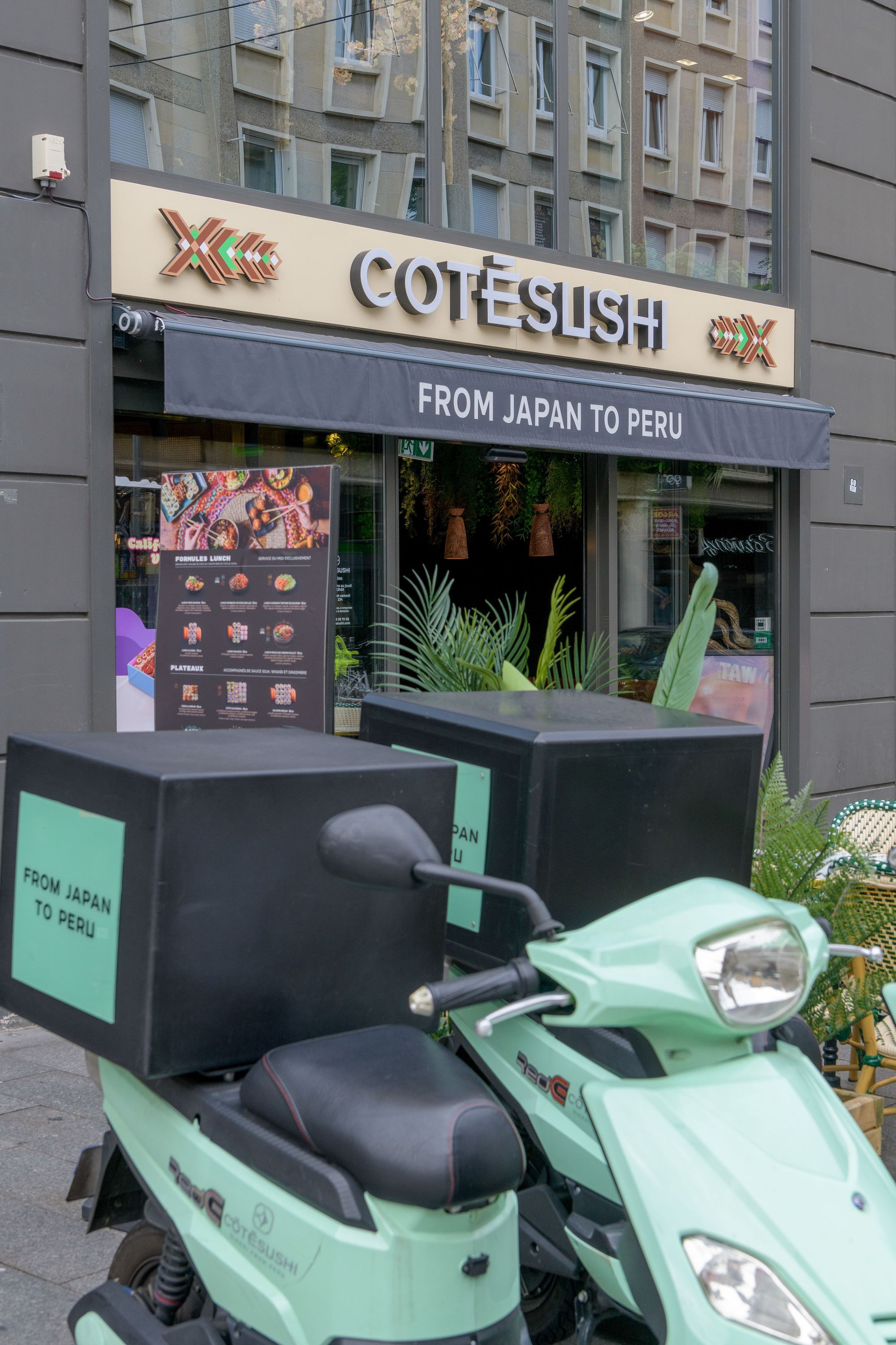 Façade du restaurant japonais Côté Sushi Mulhouse avec un scooter de livraison, enseigne et panneaux publicitaires visibles.