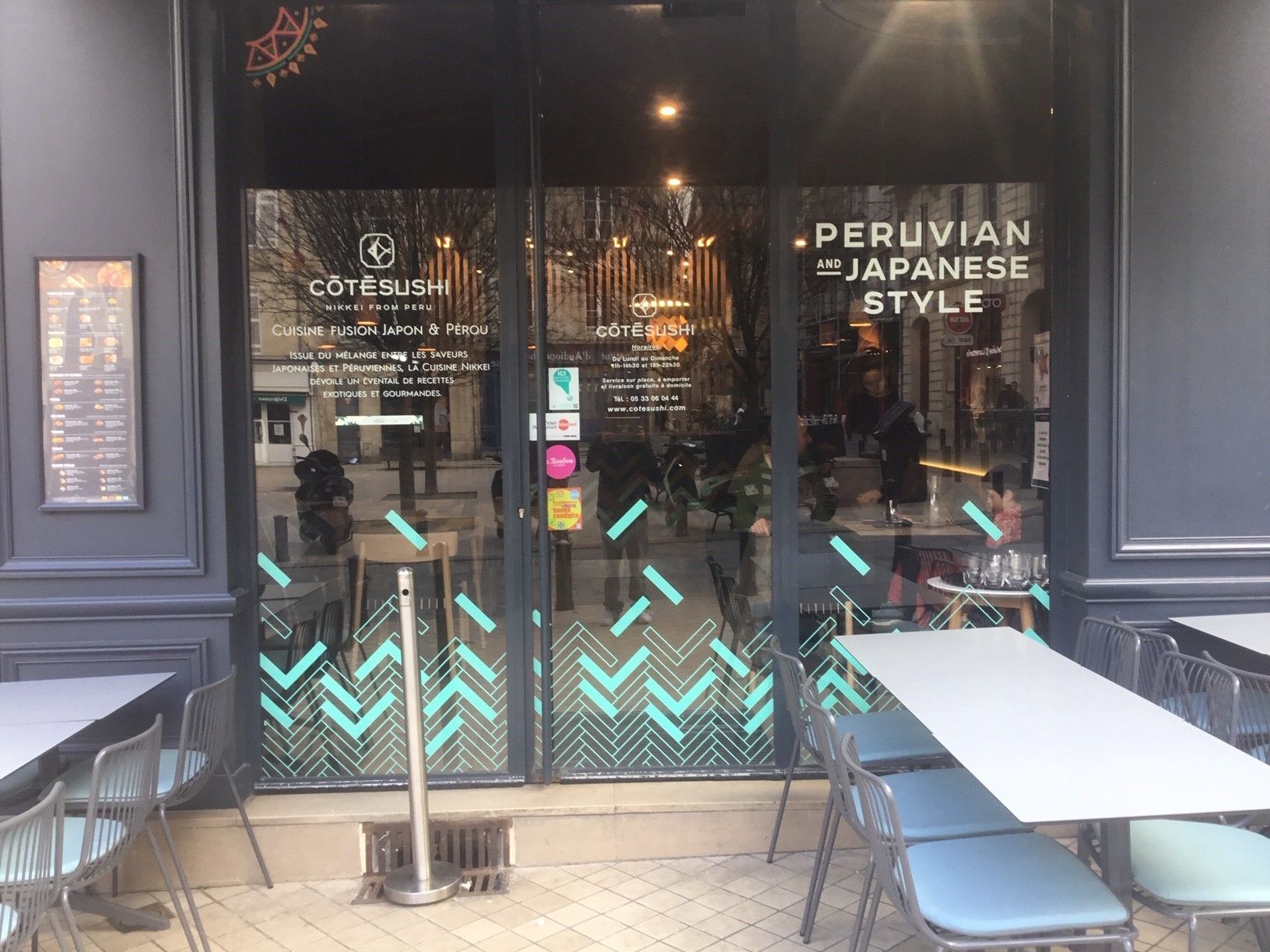 Façade du restaurant Côté Sushi Bordeaux avec sa porte en verre et des tables extérieures blanches avec chaises métalliques.