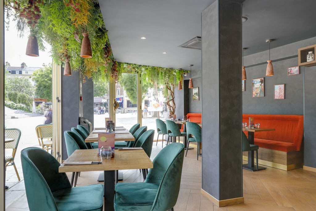 Intérieur moderne de restaurant japonais avec chaises vertes, banquettes rouges et décor végétal suspendu près des fenêtres.