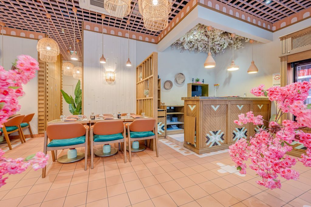 Intérieur moderne de restaurant japonais à Montpellier avec tables, chaises, décorations florales et comptoir en bois.