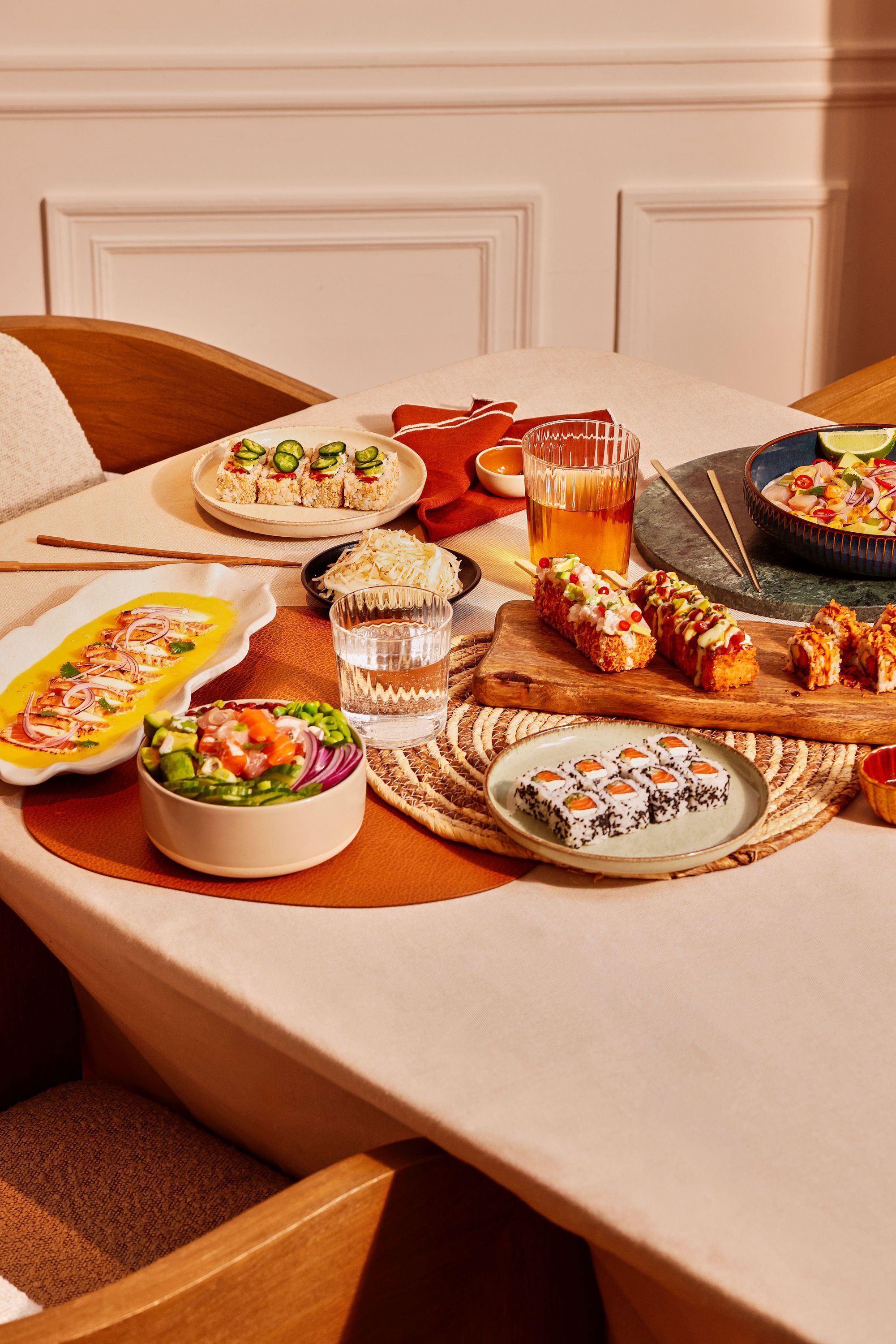 Plateaux de sushi variés et boissons sur table beige avec chaises en bois dans restaurant japonais.