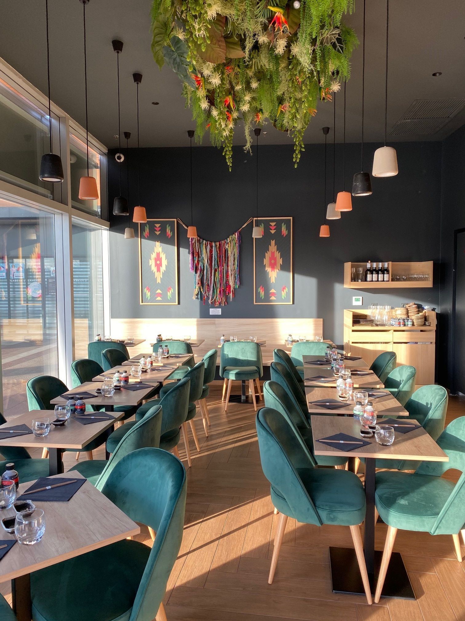 Salle de restaurant japonais avec tables en bois, chaises vertes, luminaires suspendus et décorations murales colorées.
