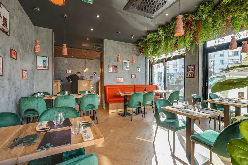 Intérieur du restaurant Côté Sushi Aix-en-Provence avec tables en bois, chaises vertes et décorations végétales suspendues.