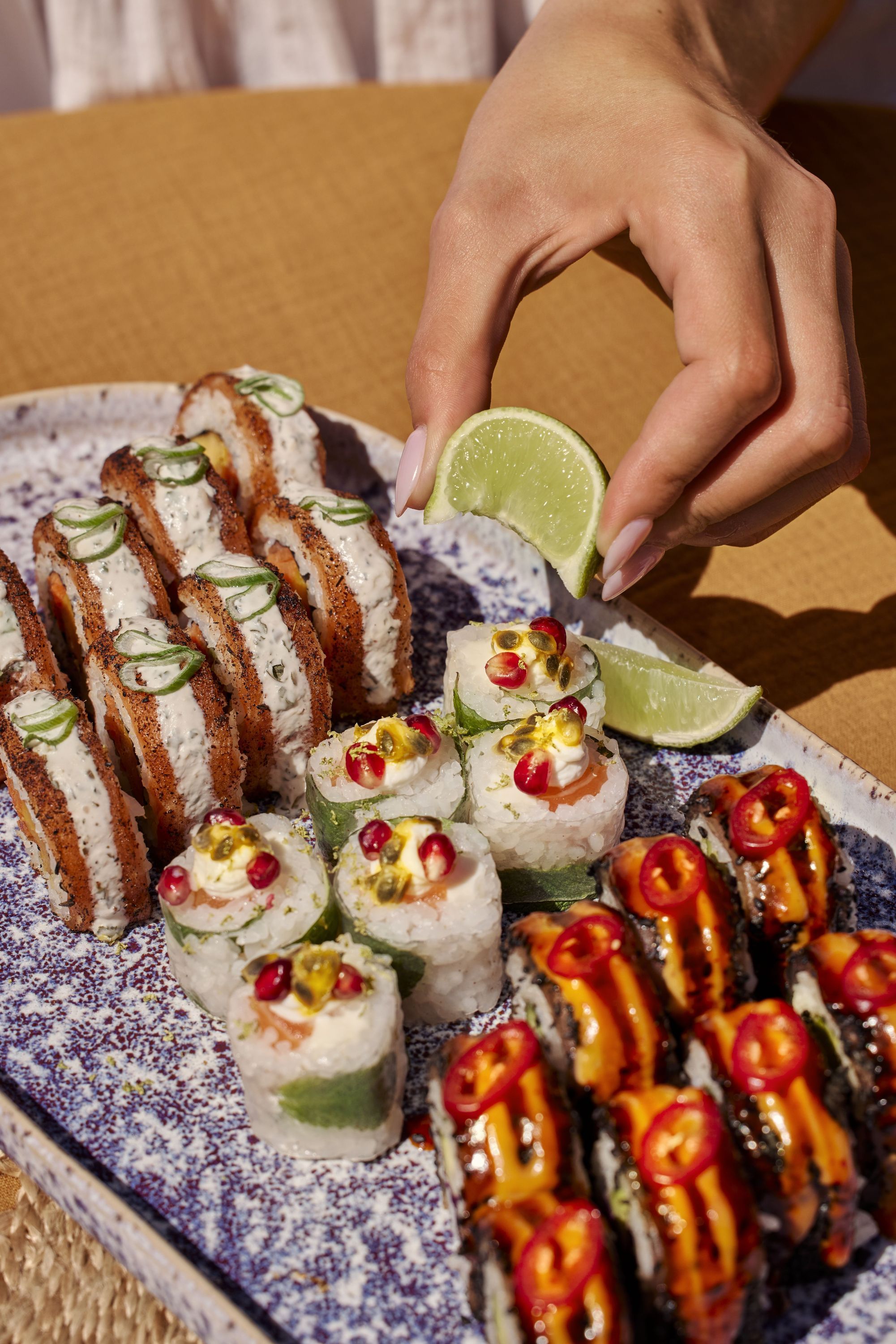 Assortiment de sushi variés avec une main pressant un quartier de citron vert sur une assiette.