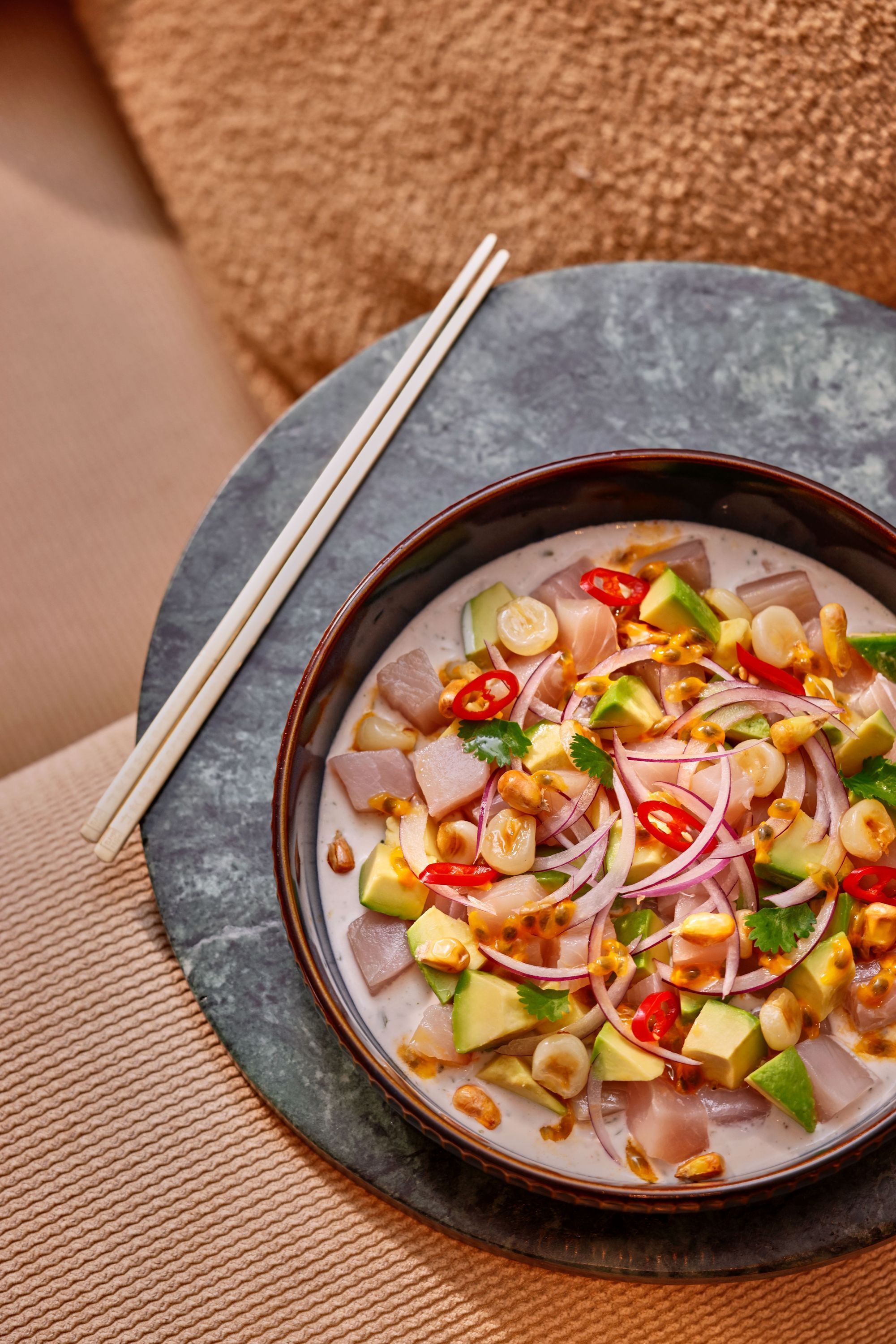 Bol de ceviche japonais frais avec avocat, oignon rouge, piment, coriandre et maïs grillé, servi avec des baguettes.