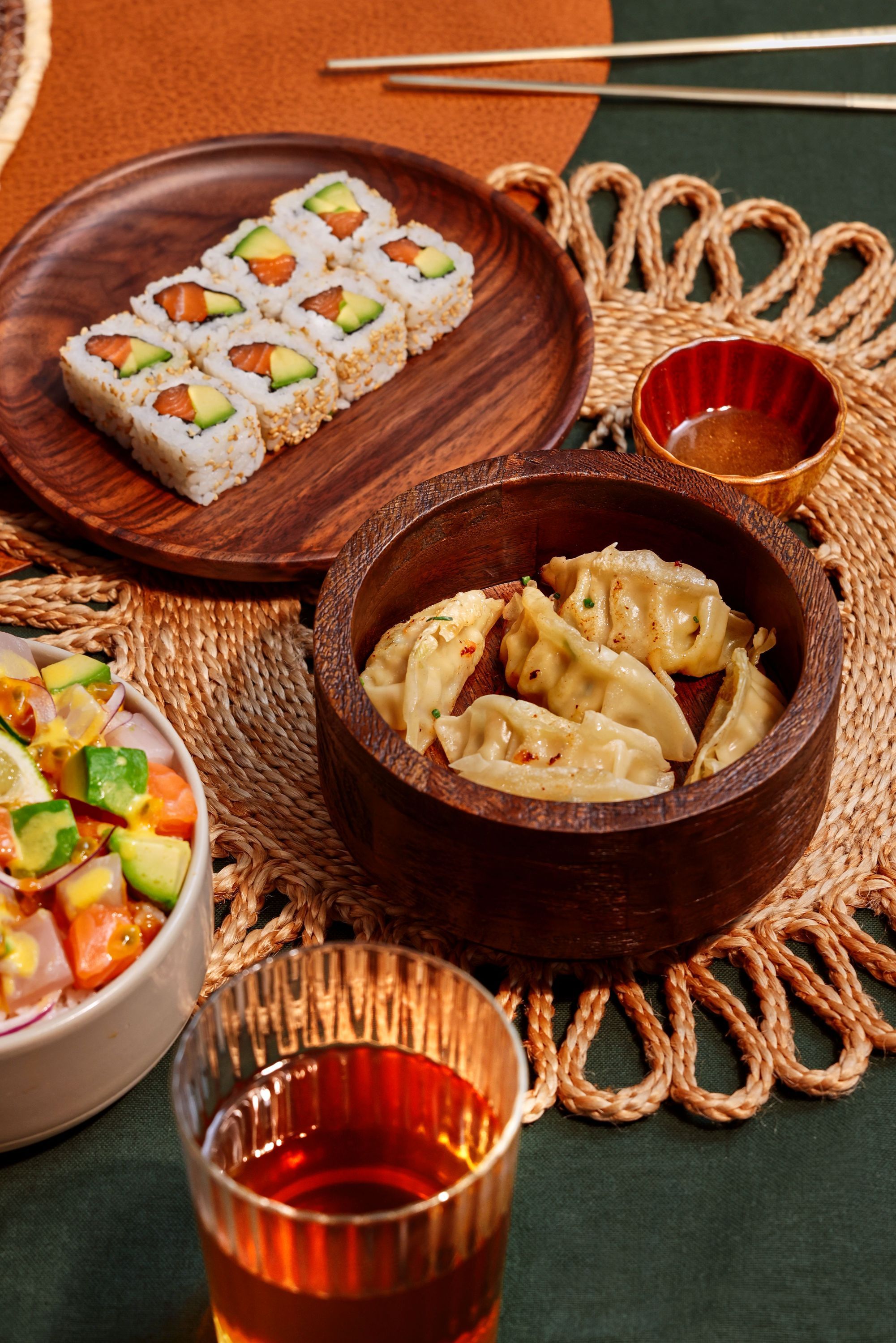 Assortiment de sushis et raviolis dans un restaurant japonais avec une boisson sur une table tissée.