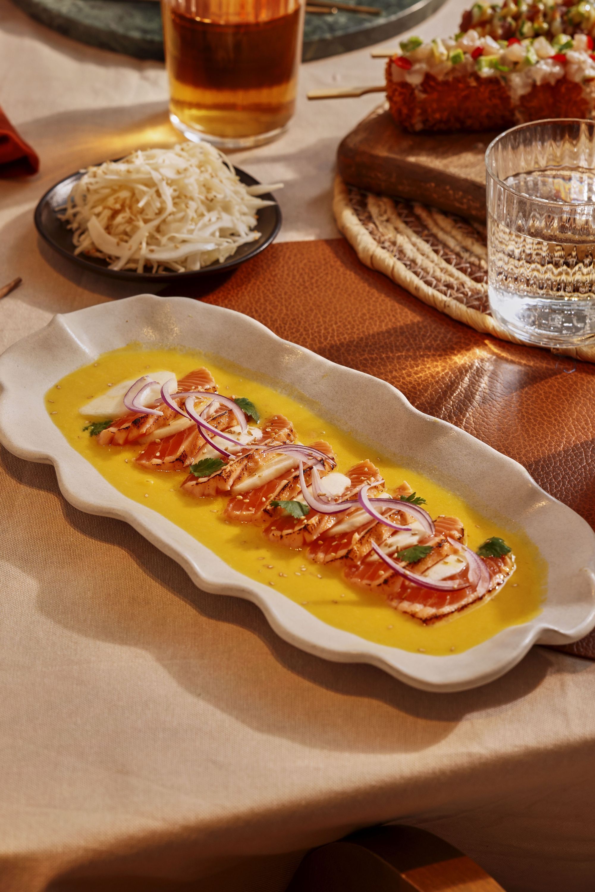 Tranches de sushi nappées d'une sauce jaune, accompagnées de légumes et présentées sur une grande assiette blanche.