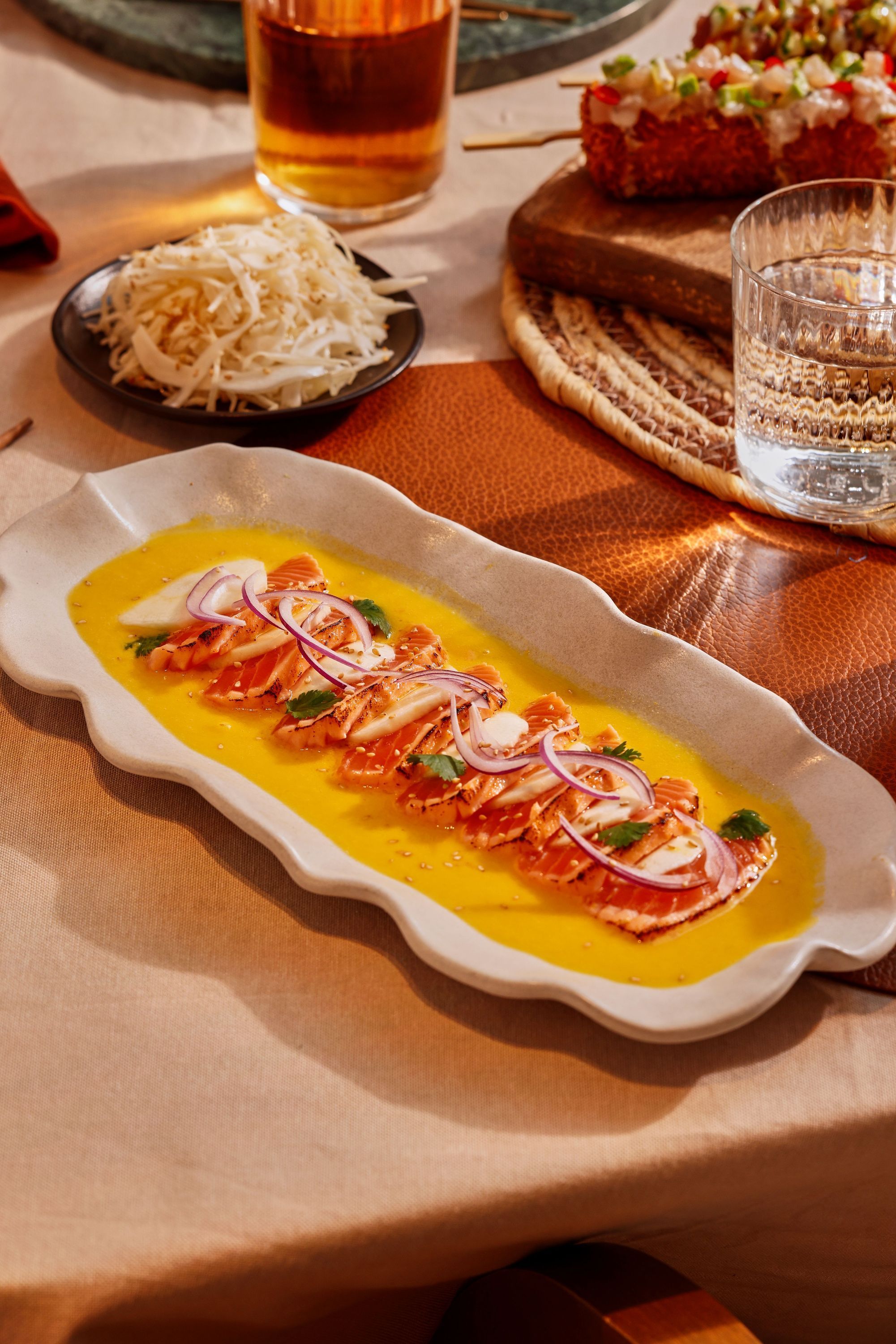 Sashimis de saumon nappés de sauce et garnis d'oignons rouges, servis sur une assiette allongée dans un restaurant japonais.