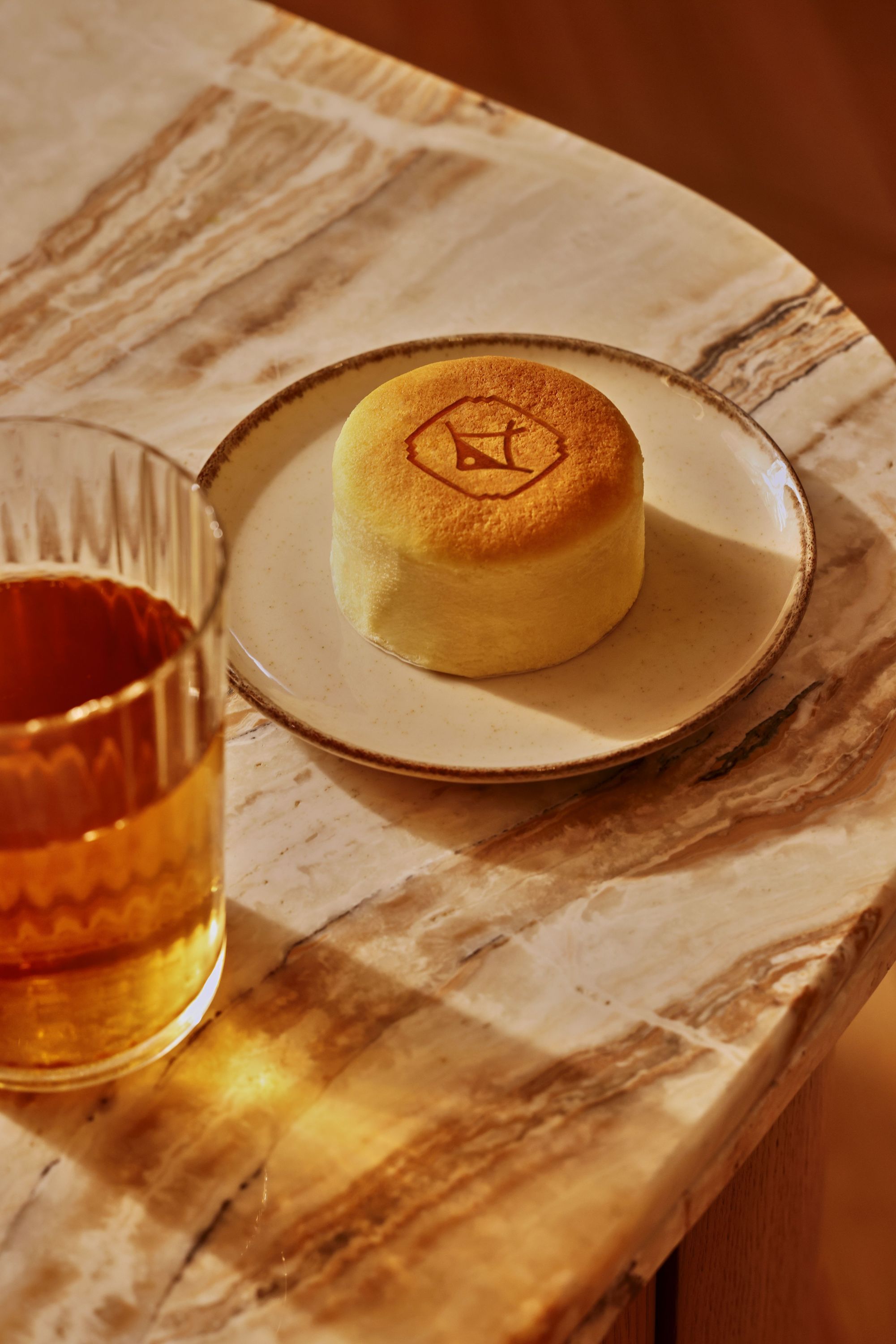 Petit gâteau japonais sur une assiette avec une boisson dans un verre en verre sur une table en bois clair.